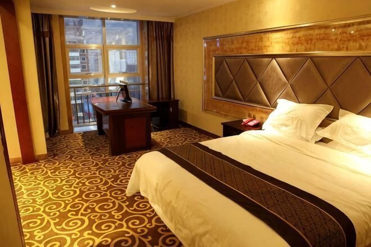 Quarto de hotel com uma cama grande, uma escrivaninha e vista da cidade pela janela.