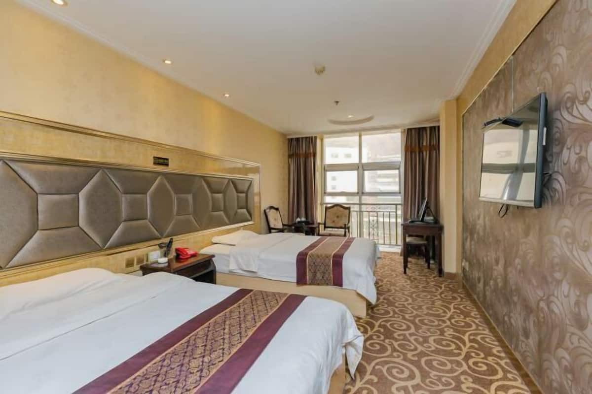 Quarto de hotel com duas camas, uma cabeceira grande, televisão de tela plana, uma escrivaninha e vista para a cidade.