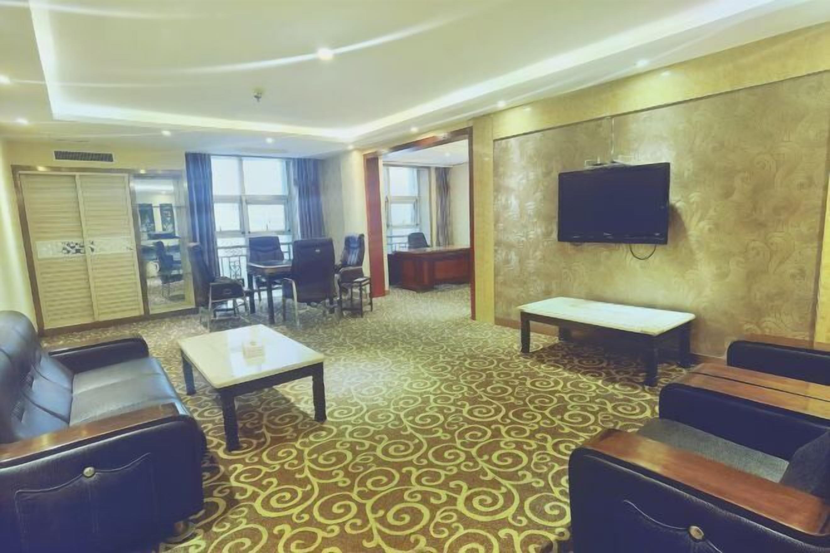 A hotel lobby with a patterned carpet, leather seating, a television, and a dining area.