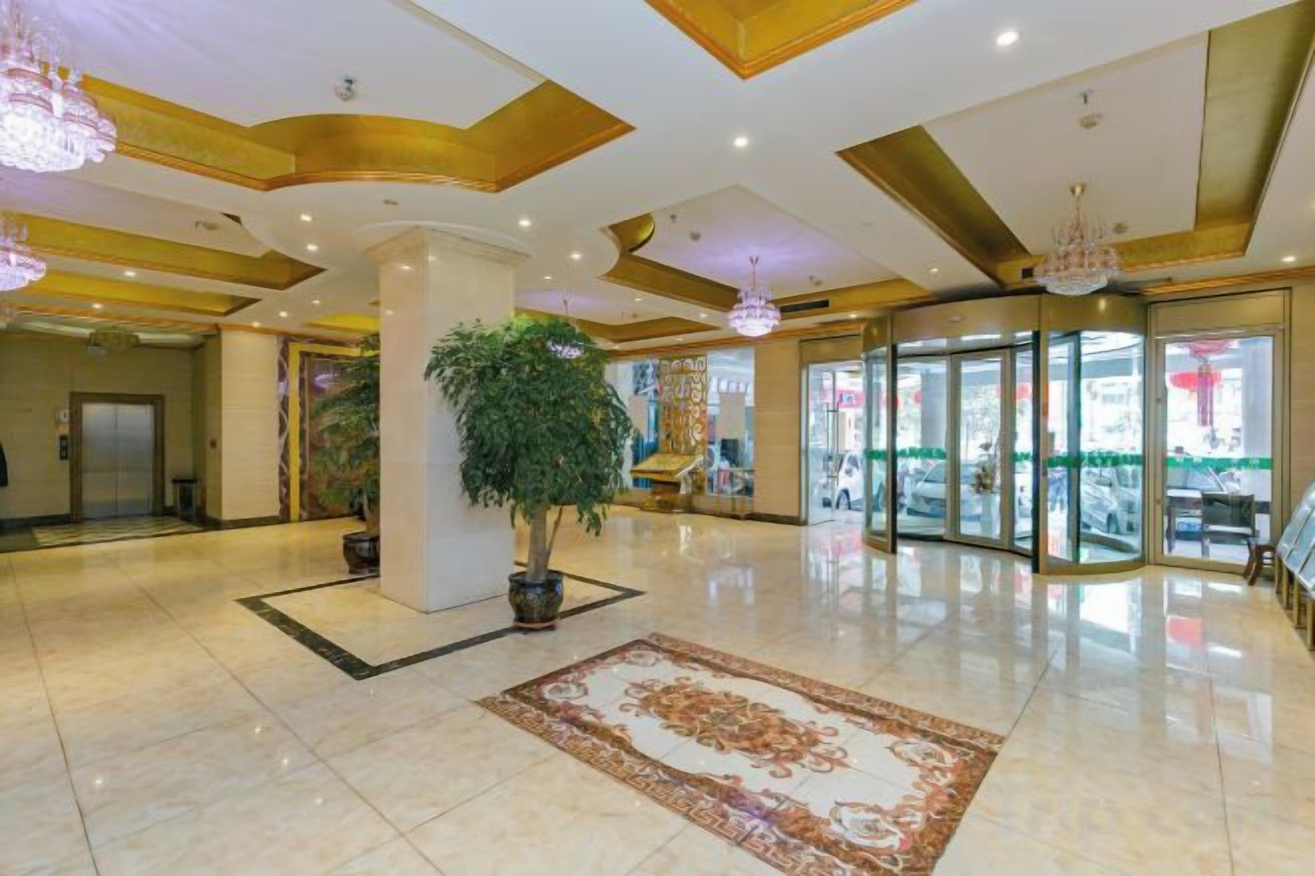 A hotel lobby with a marble floor, a large potted plant, a patterned rug, and a revolving door.