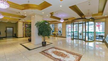 A hotel lobby with a marble floor, a large potted plant, a patterned rug, and a revolving door.