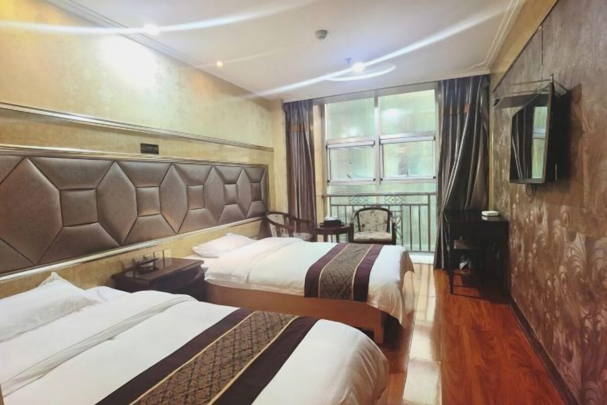 A hotel room with two beds, a large window with curtains, a television mounted on the wall, and a small table with a chair.
