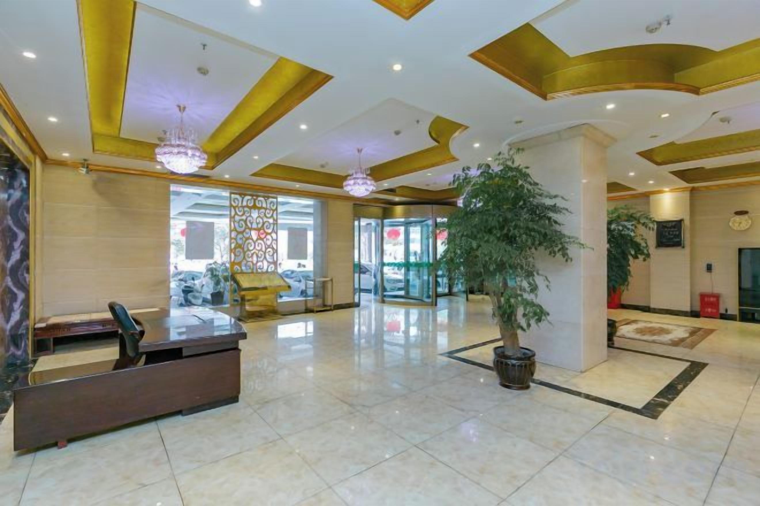 A hotel lobby with a reception desk, a large potted plant, and a chandelier.