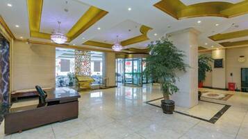 Un vestíbulo de hotel con una recepción, una planta en maceta grande y un candelabro.