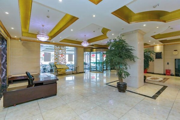 A hotel lobby with a reception desk, a large potted plant, and a chandelier. - Bright Pearl Hotel (Longnan)