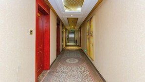 Ein Hotelkorridor mit gemustertem Teppich, roten Türen und einer Decke mit geometrischem Muster.