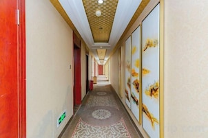 Un pasillo de hotel con alfombra estampada, obras de arte enmarcadas en las paredes y una puerta roja a la izquierda.