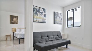 A modern living room with a grey sofa, a small wooden stool, a white lamp, and two framed artworks on the wall. - Miami Suite 310 (Miami)