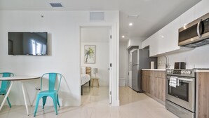 A modern kitchen with stainless steel appliances, a dining area with a table and chairs, and a hallway leading to a bedroom. - Miami Suite 310 (Miami)