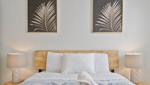 A neatly made bed with a patterned bedspread, two bedside lamps, and two framed leaf artworks on the wall. - Miami Suite 310 (Miami)