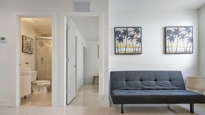 A modern living room with a sofa, a painting of palm trees, and a view into the bathroom. - Miami Suite 310 (Miami)