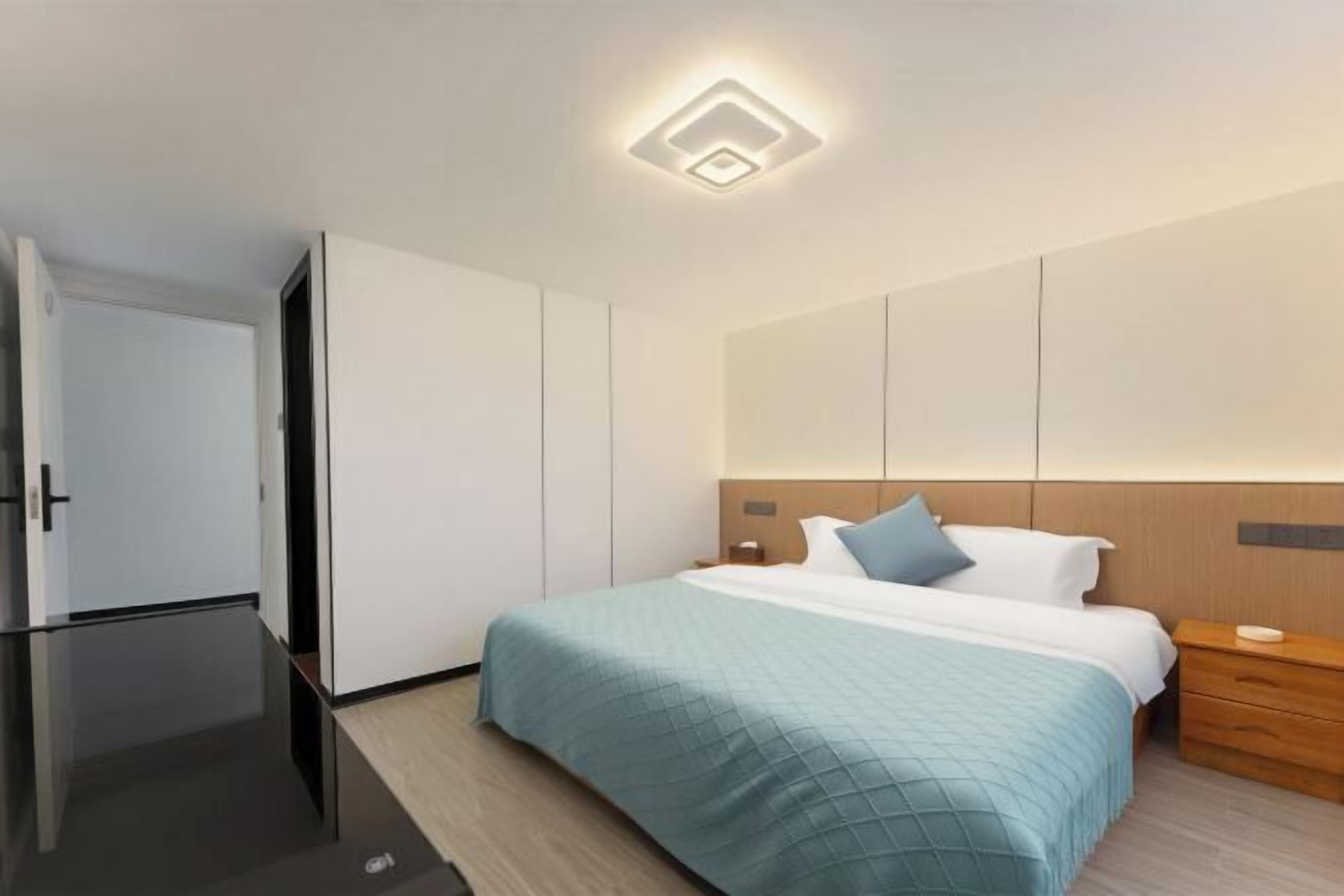 A modern hotel room with a bed, bedside table, and a wardrobe.