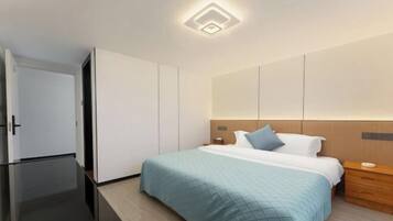 A modern hotel room with a bed, bedside table, and a wardrobe.