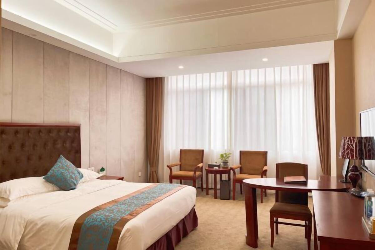 A hotel room with a bed, two armchairs, a small table, a TV, and a window with curtains.