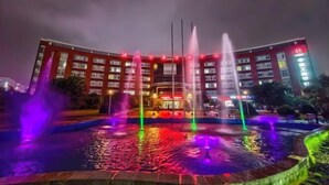 A hotel with a fountain in front, multiple floors, and illuminated signage. - International Academic Exchange Center (Yuntang Campus Hotel, CSUST) (Changsha)