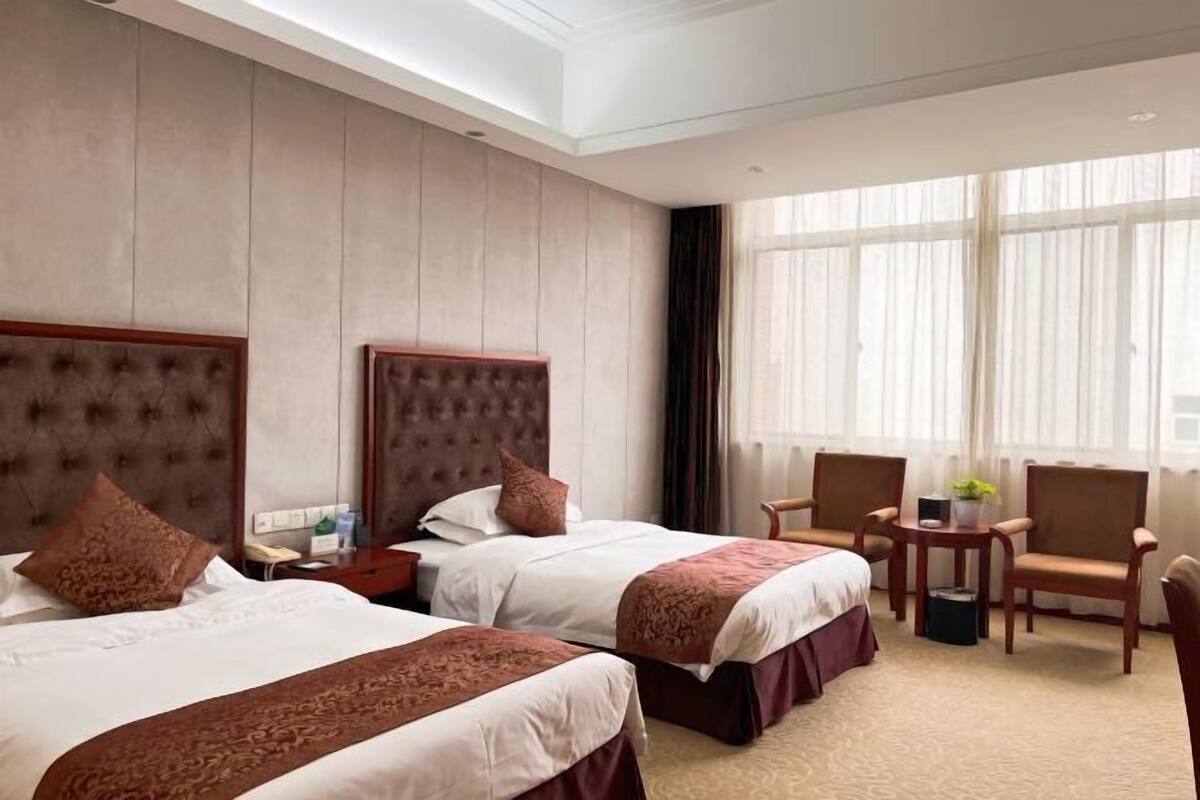 A hotel room with two beds, a sitting area with chairs, a small table, and a window with curtains.