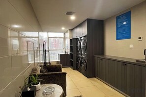 A modern kitchen with a built-in washer and dryer, a dining area with a table and chairs, and large windows offering a view of the city. - International Academic Exchange Center (Yuntang Campus Hotel, CSUST) (Changsha)
