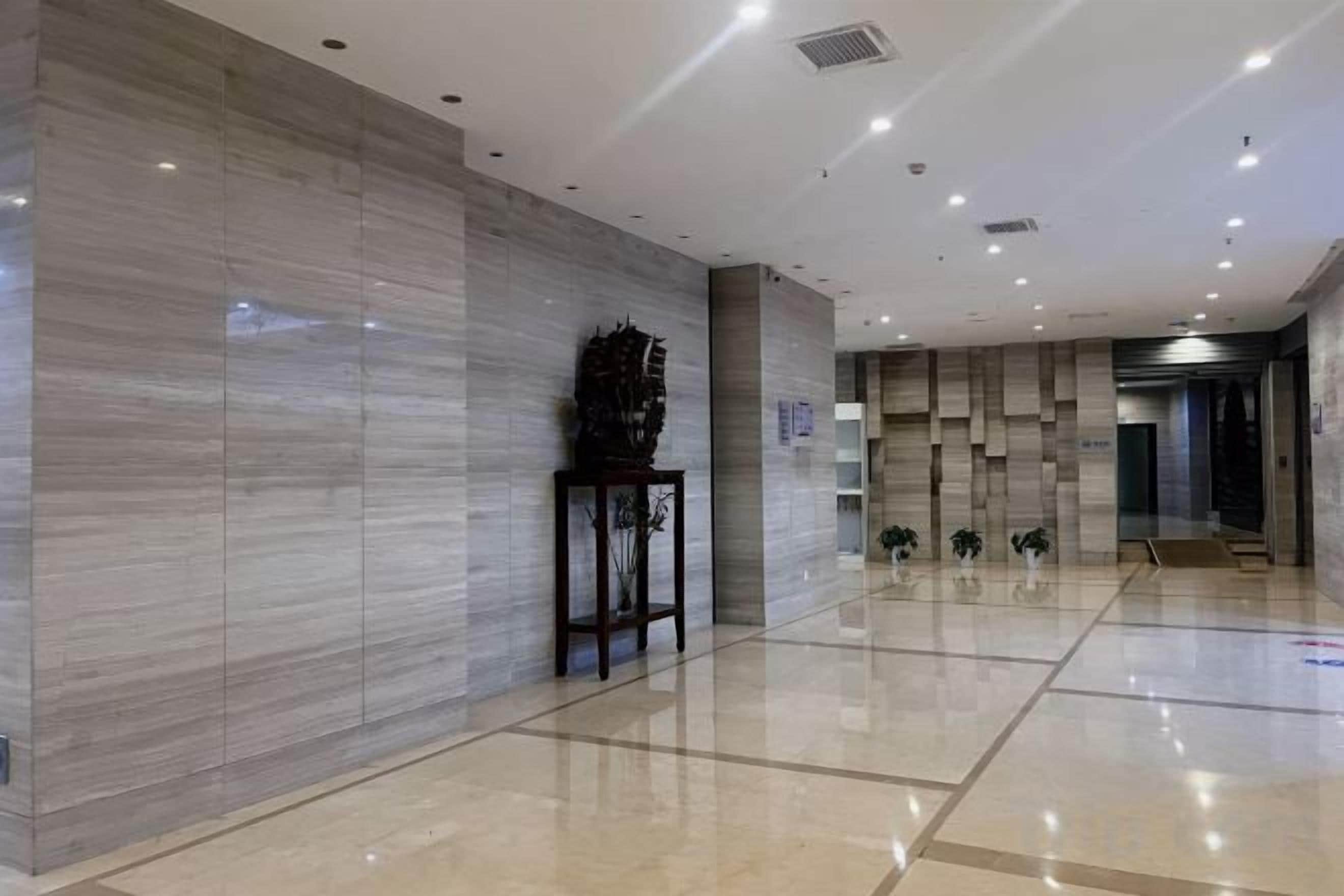 A spacious lobby with a marble wall, a reception desk, and a plant arrangement.