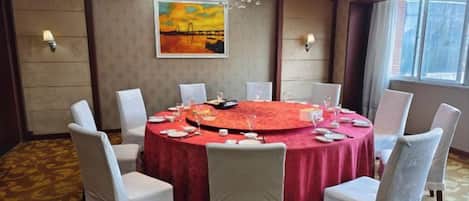 Un salón de conferencias con una mesa redonda, sillas blancas y un mantel rojo.