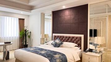 A hotel room with a large bed, a bedside table with a lamp, a mirror, and a window with curtains.