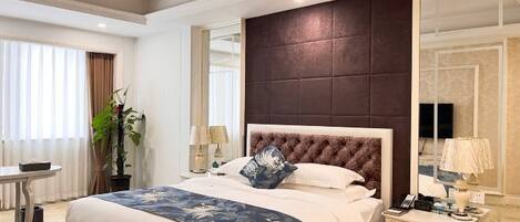 A hotel room with a large bed, a bedside table with a lamp, a mirror, and a window with curtains.