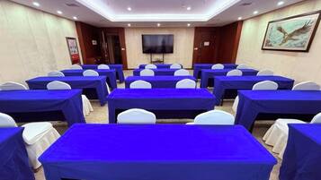 A conference room with rows of tables and chairs, a flat-screen TV, and a painting on the wall.