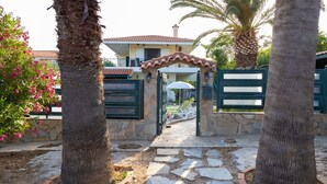 A stone pathway leading to a gated entrance with a tiled roof and a small patio area with a table and chairs. - Villa Rose (Anavissos)