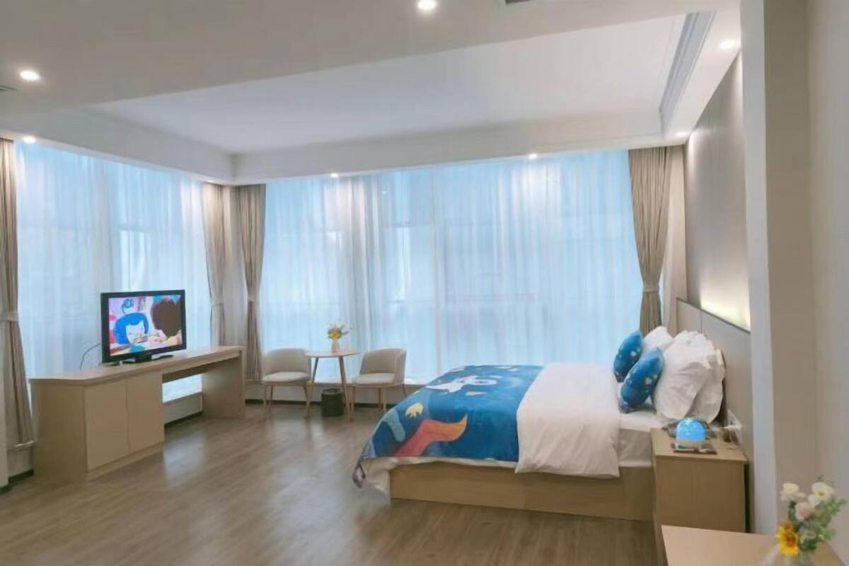 Quarto de hotel com cama, televisão, secretária e cadeira.