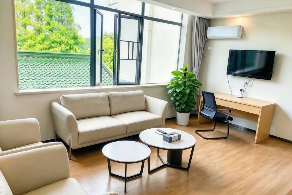 A modern living room with a sofa, two coffee tables, a TV, and a large window with a view of greenery.