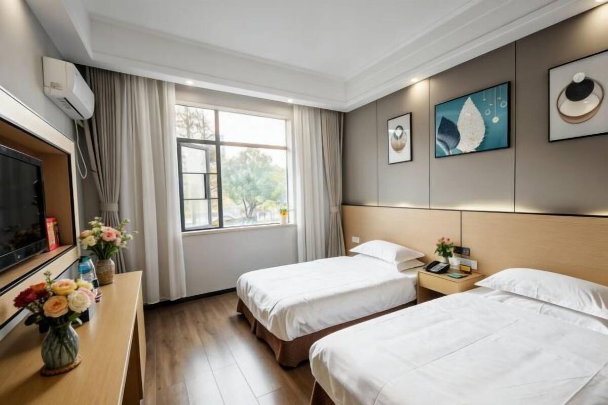 Quarto de hotel com duas camas, televisão, escrivaninha com um vaso de flores e obras de arte nas paredes.