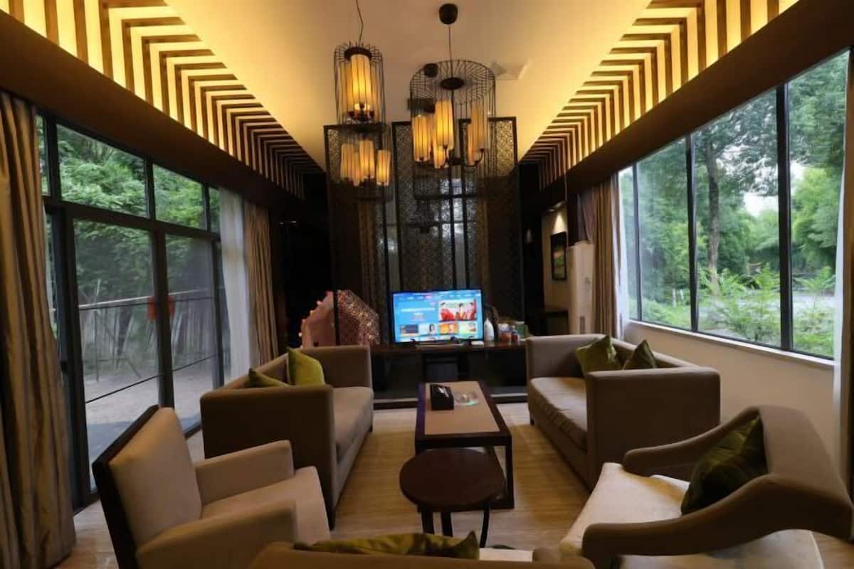 Uma sala de estar moderna com uma TV grande, assentos confortáveis e amplas janelas com vista para o exterior.