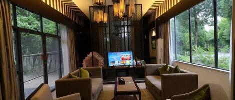 A modern living room with a large TV, comfortable seating, and large windows offering a view of the outdoors.