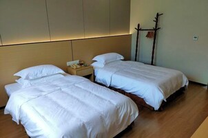 Habitación de hotel con dos camas individuales, suelo de madera, mesita de noche con teléfono y perchero en la pared.