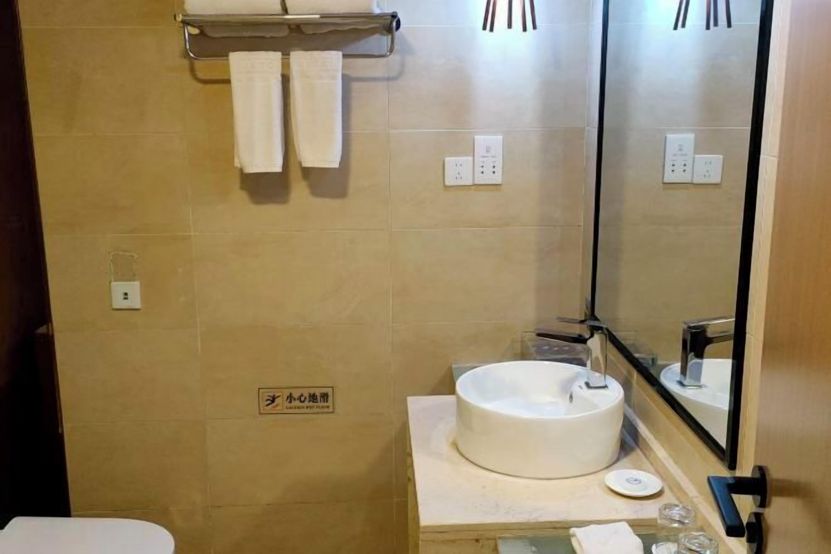 Un bagno con lavandino, specchio, porta asciugamani e un cartello appeso al muro.