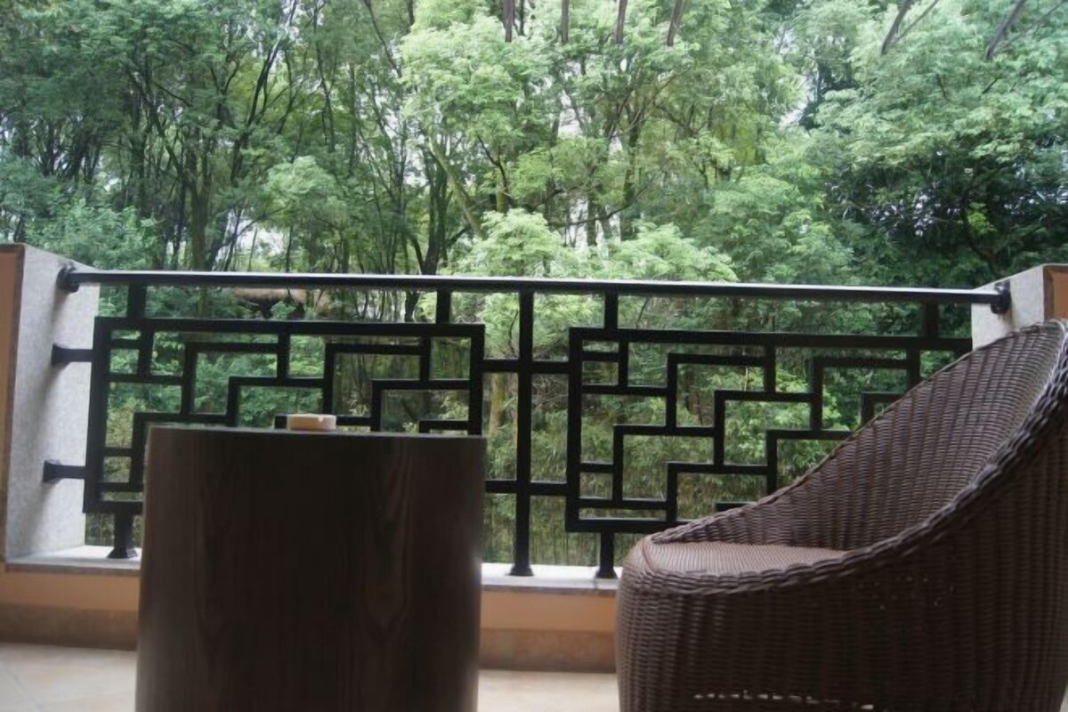 A balcony with a wicker chair and a wooden table, overlooking a lush green forest.