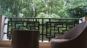 Un balcón con una silla de mimbre y una mesa de madera, con vista a un bosque verde y frondoso.