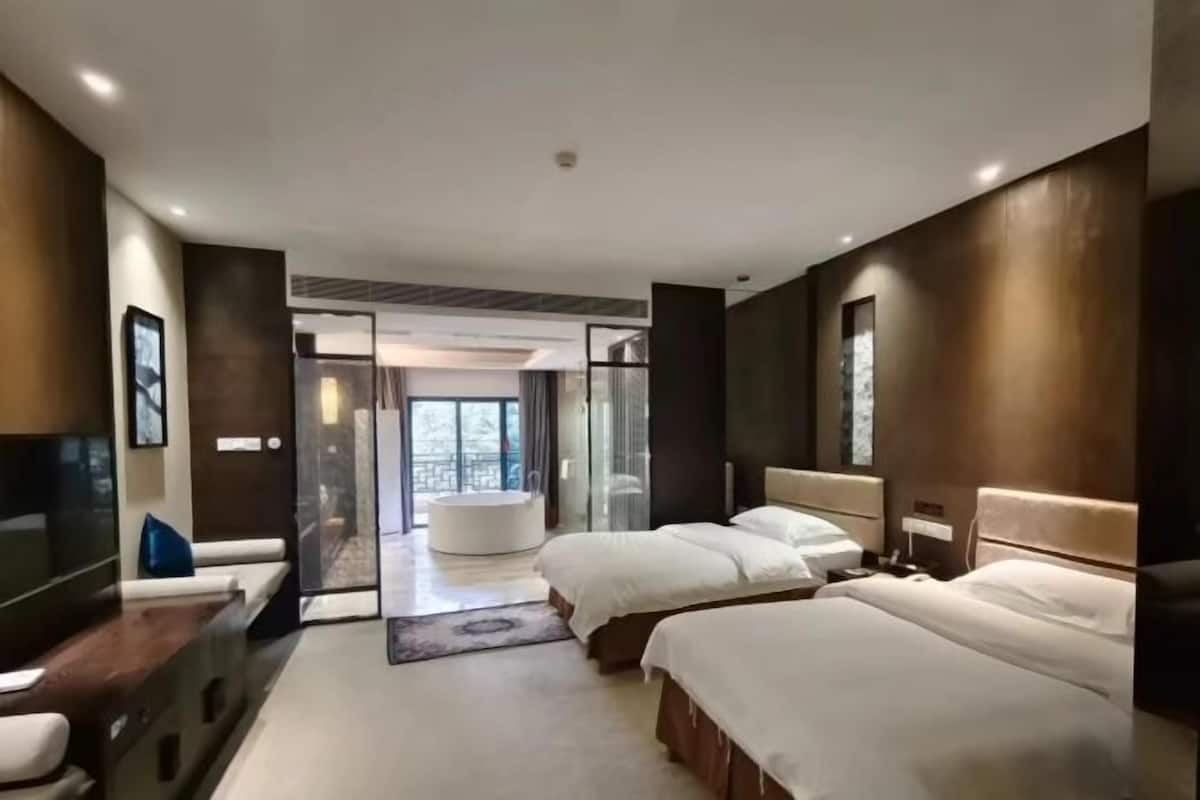 Quarto de hotel moderno com duas camas, televisão e porta de vidro para uma varanda.