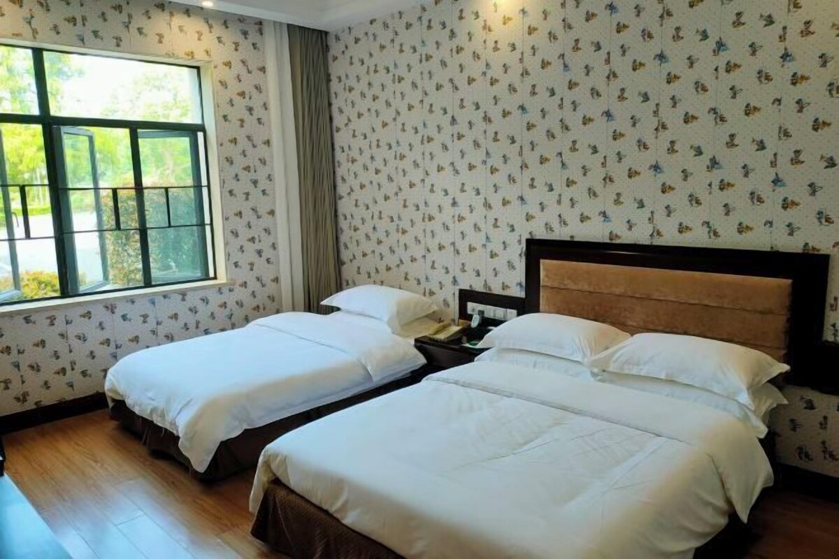 A hotel room with two beds, a window, and patterned wallpaper.