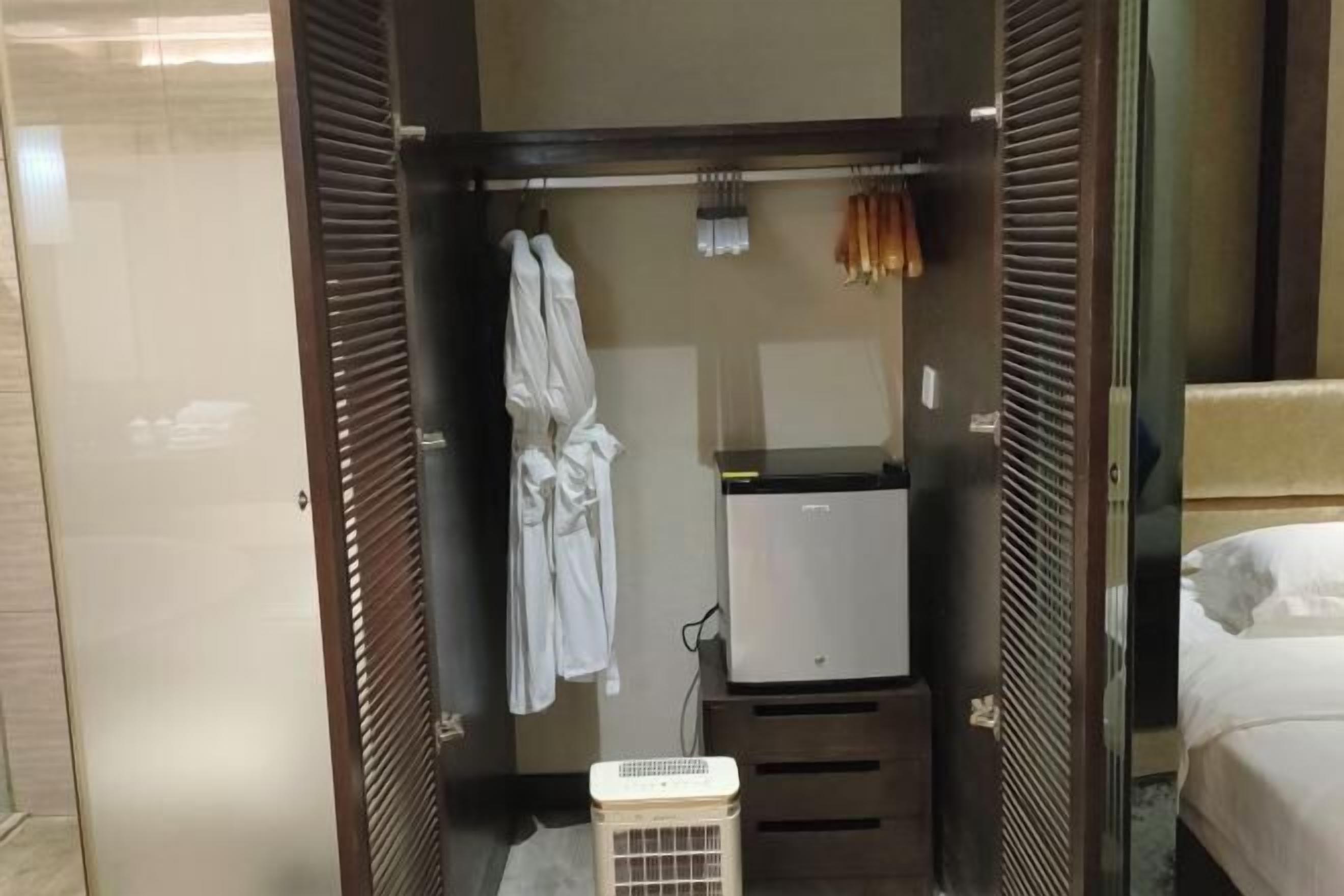 Une chambre d’hôtel dotée d’un dressing où se trouvent un peignoir blanc, un radiateur et un petit réfrigérateur.