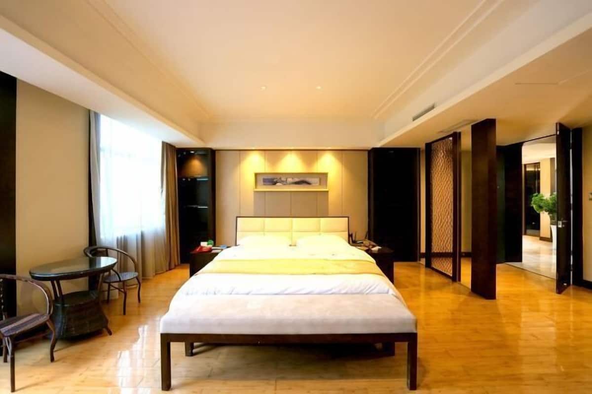 Quarto de hotel com uma cama grande, mesas de cabeceira, uma escrivaninha e uma cadeira.