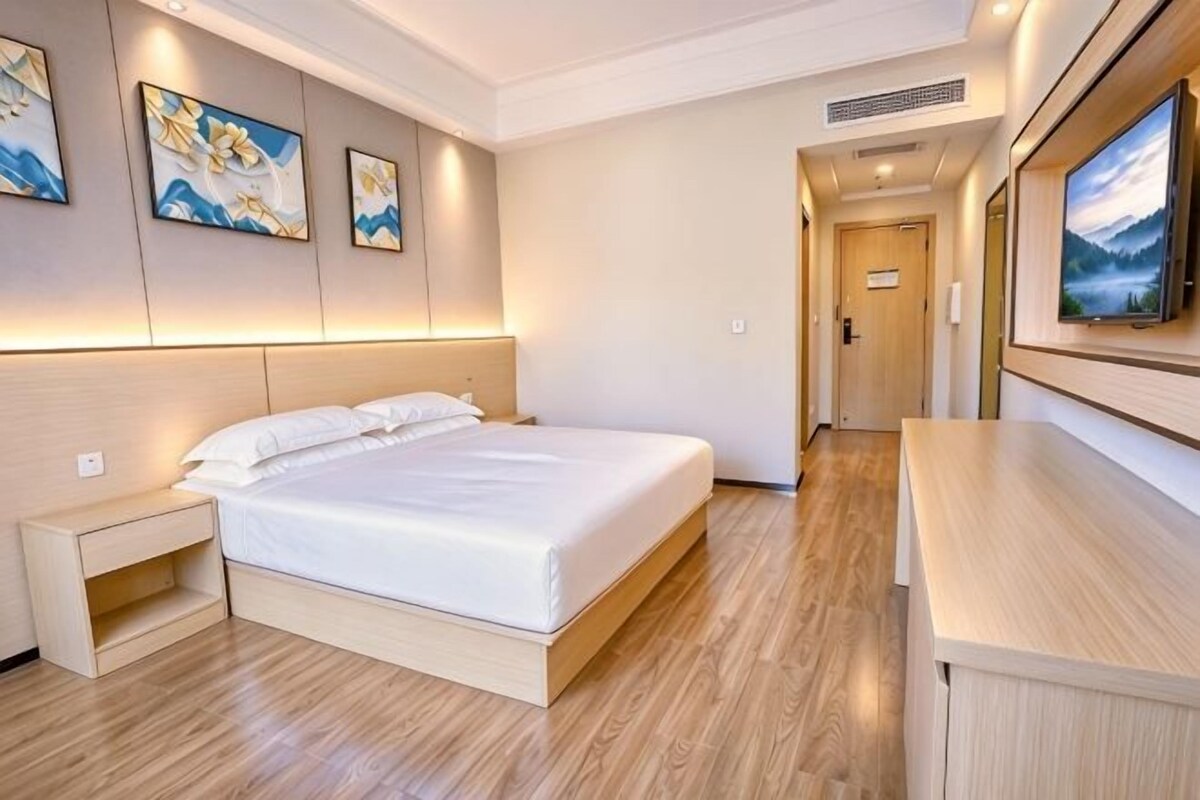 A hotel room with a bed, bedside table, artwork on the walls, and a TV.