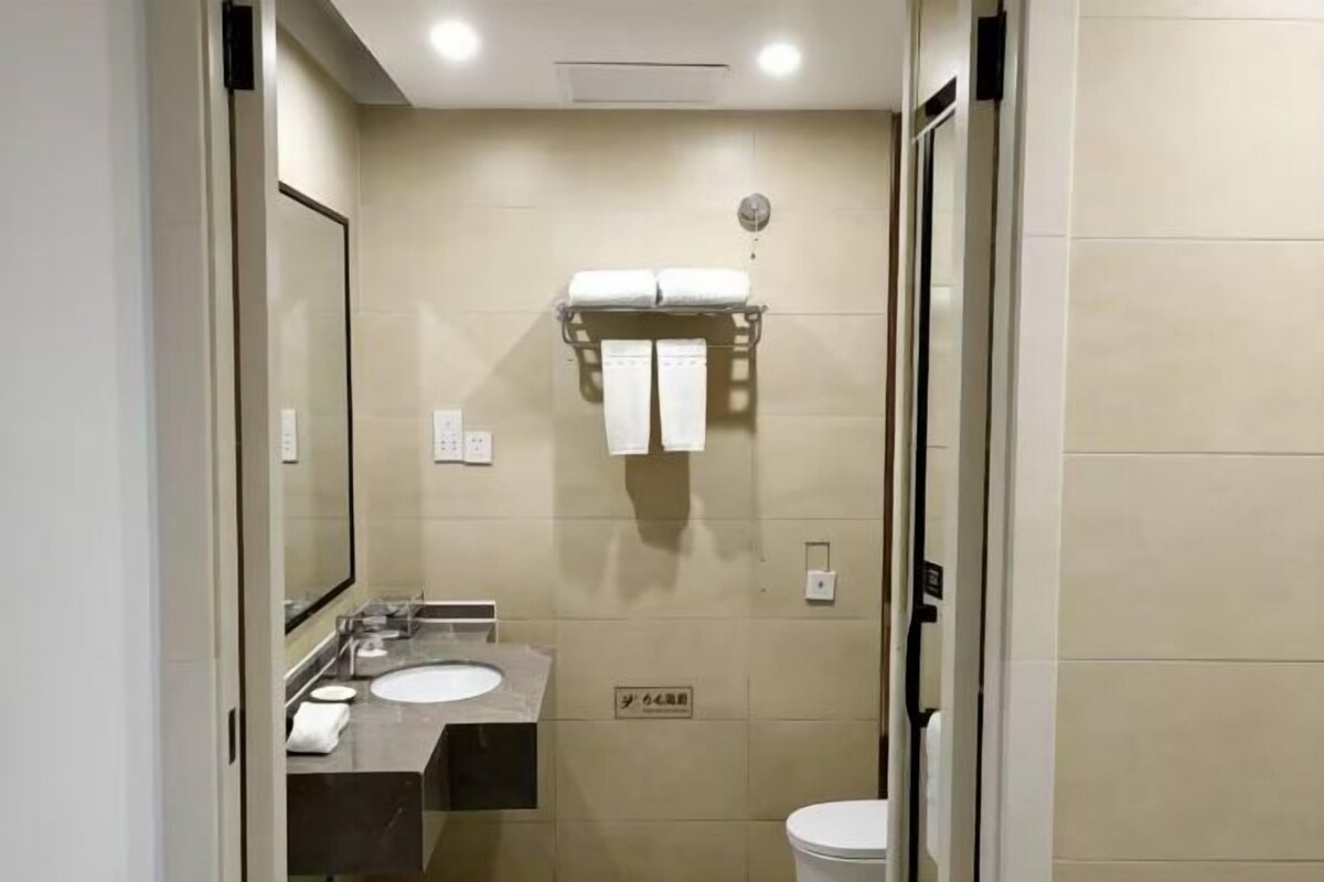 A modern bathroom with a sink, mirror, and toilet. There are towels hanging on a rack.
