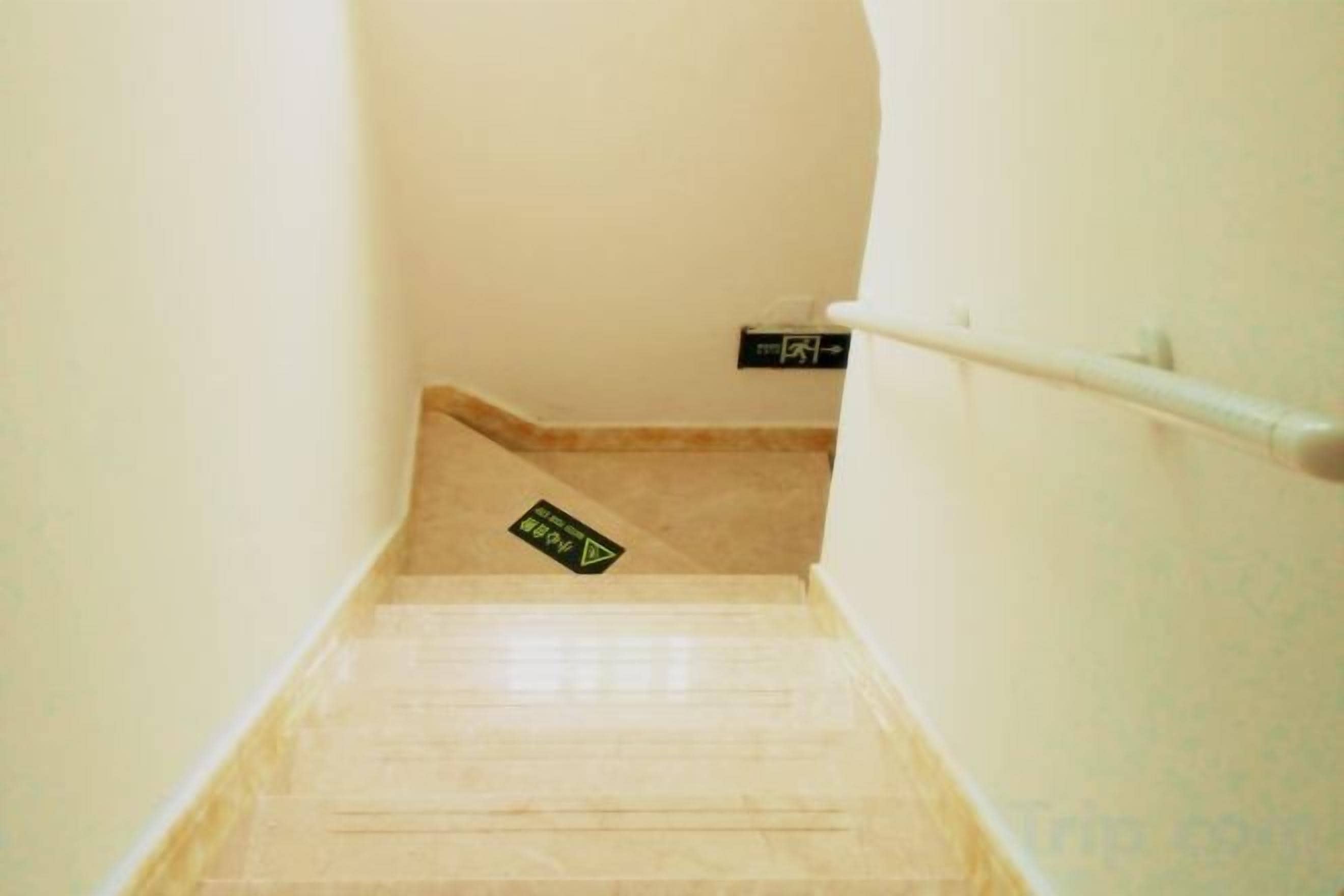 A narrow stairway with a handrail, a sign on the wall, and a carpeted landing.