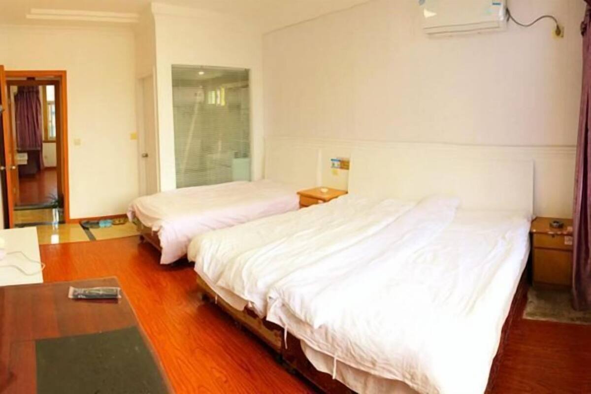 Une chambre d’hôtel avec deux lits simples, un plancher en bois, une petite table et une fenêtre avec des rideaux.