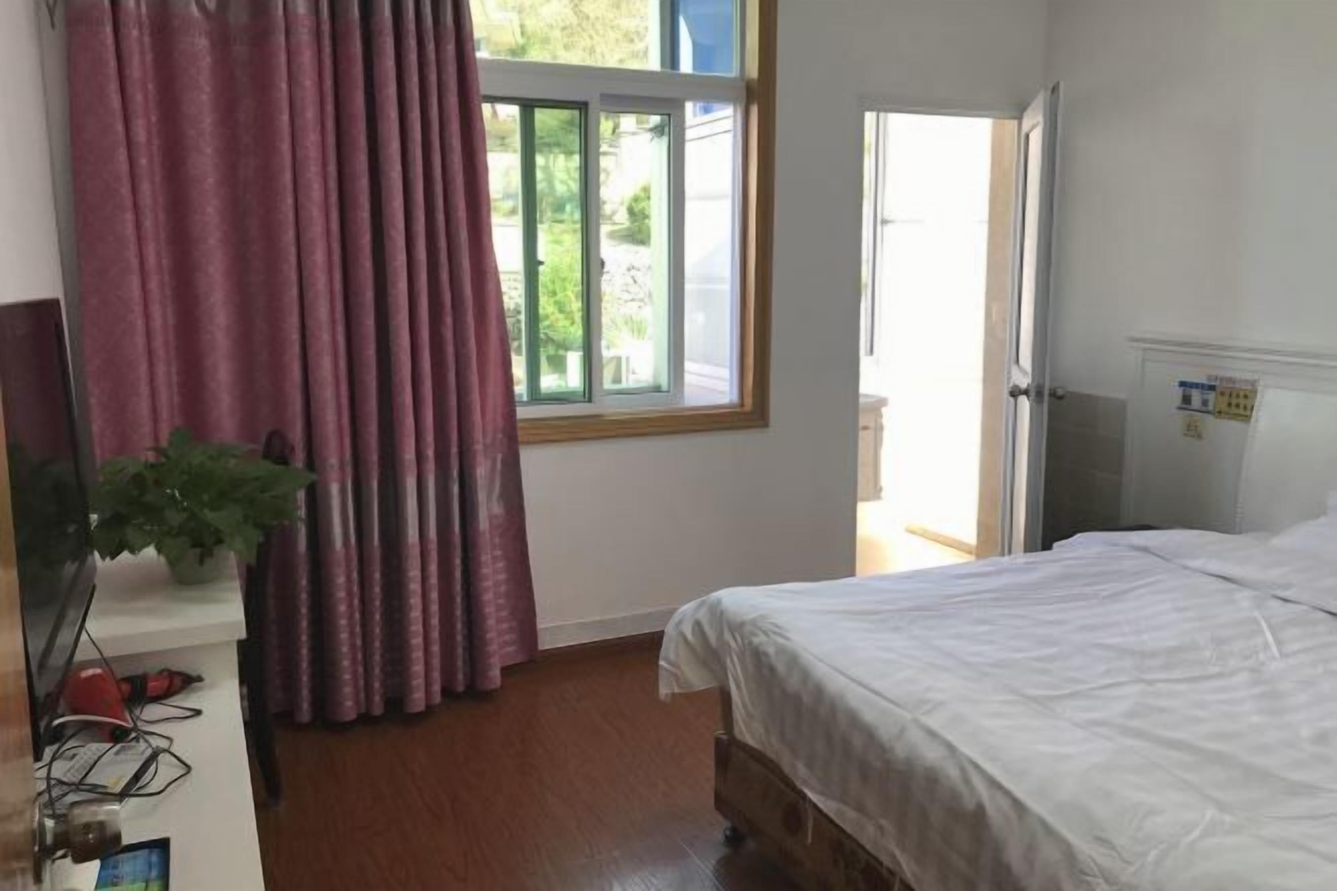 Un dormitorio con cama, ventana con cortinas, puerta y una mesita con una planta.