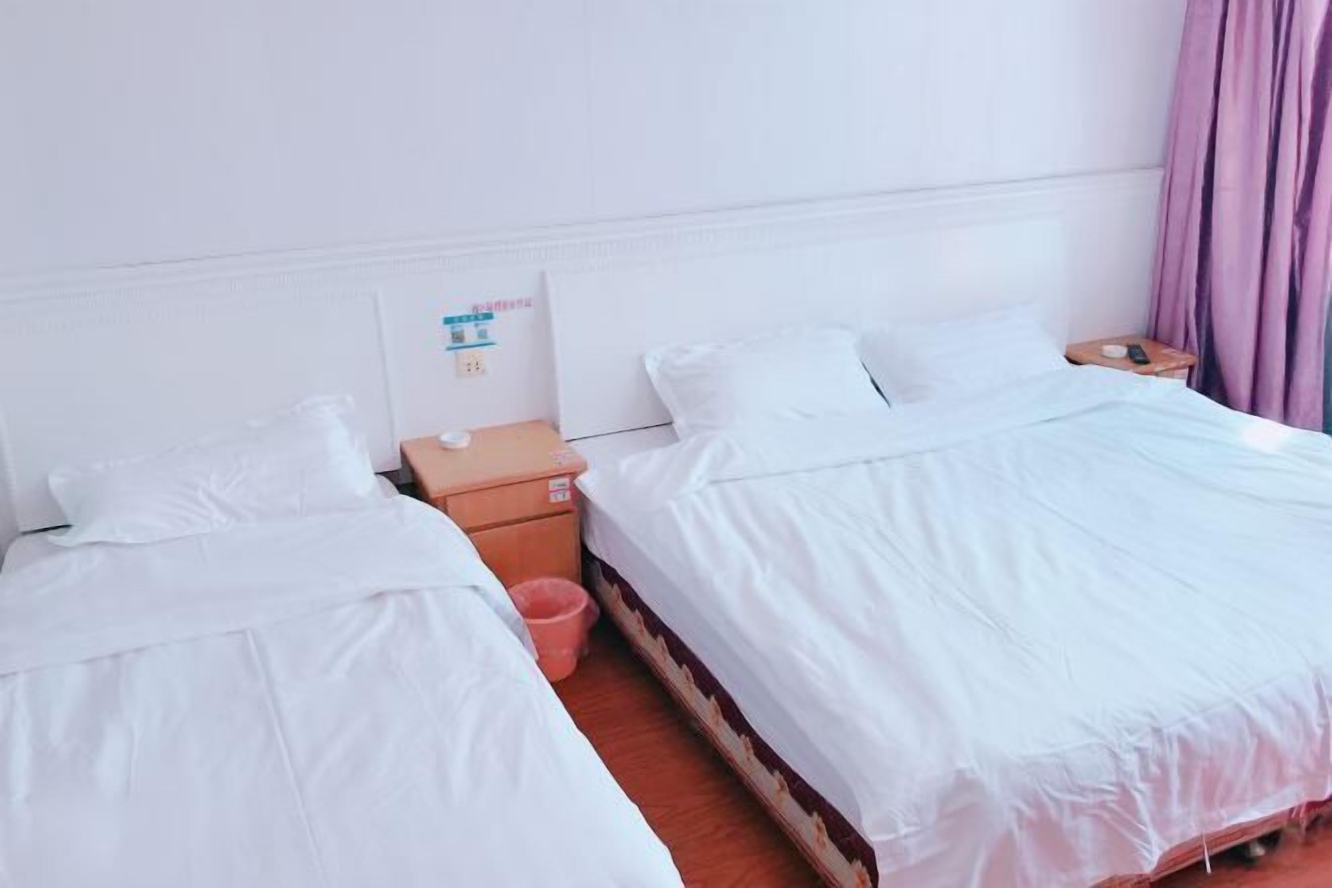 Habitación de hotel con dos camas individuales, una mesita de noche de madera, un cesto de basura y un panel de control en la pared.
