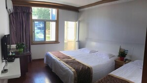 Ein Hotelzimmer mit zwei Betten, einem Schreibtisch mit Computer, einem Fenster mit Vorhängen und einem kleinen Tisch mit Pflanze.