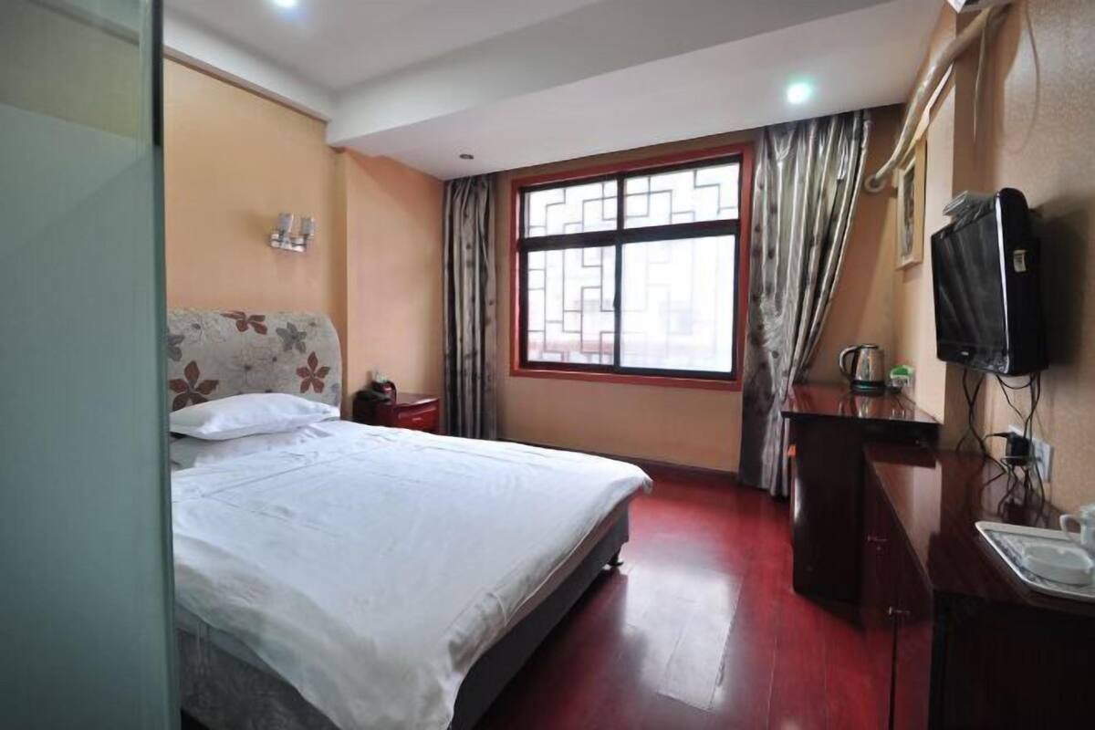 Une chambre d’hôtel avec un lit, une télévision, un bureau avec un lavabo et une fenêtre avec des rideaux.