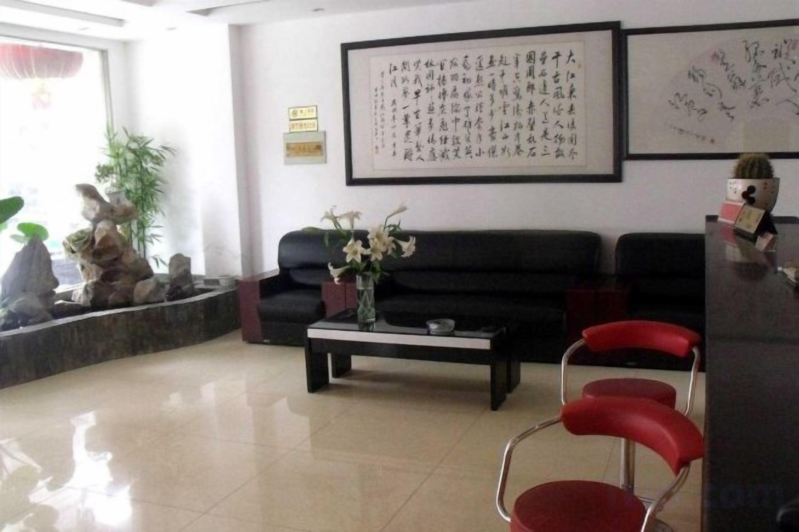 A reception area with a black sofa, a coffee table, and a red chair. There is a framed calligraphy artwork on the wall.