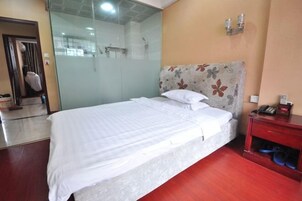 Habitación de hotel con cama, cabina de ducha de vidrio, mesita de noche de madera y teléfono instalado en la pared.